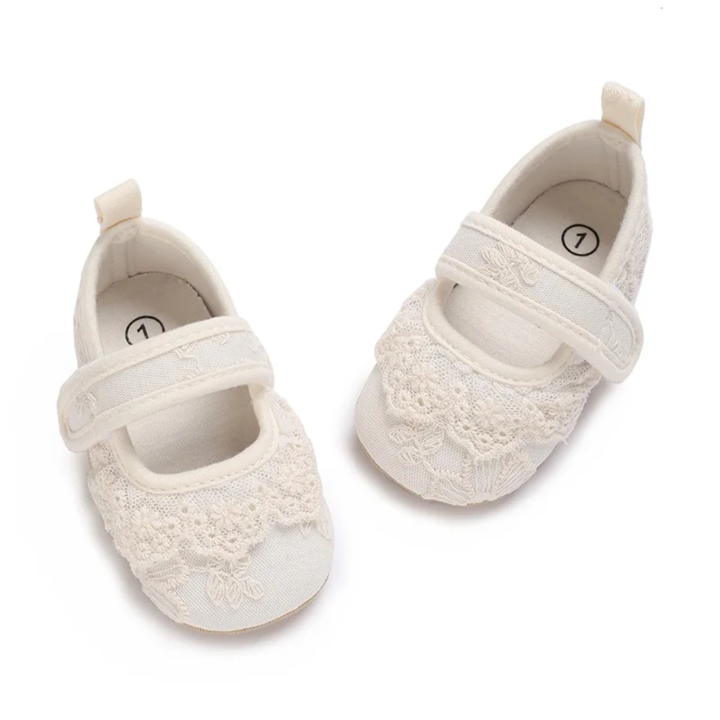 Top view of white lace baby shoes with strap closures and heel loops