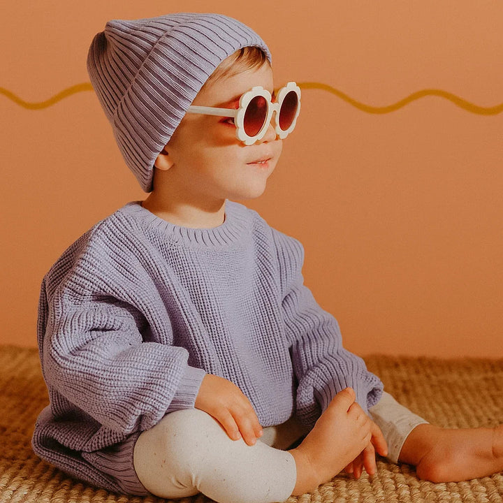 Child in a lavender knit sweater, ribbed beanie, and round sunglasses.