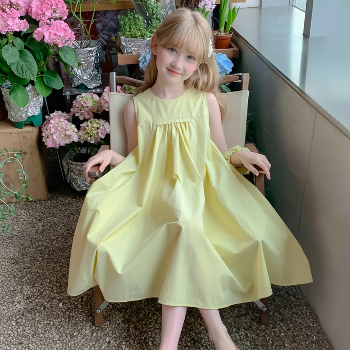 Girl holding out the skirt of a lemon-yellow sleeveless dress while seated