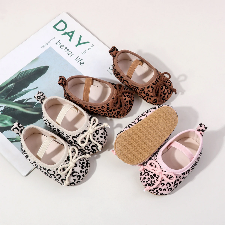 White, brown, and pink leopard-print baby shoes with elastic straps, front bows, and a textured sole