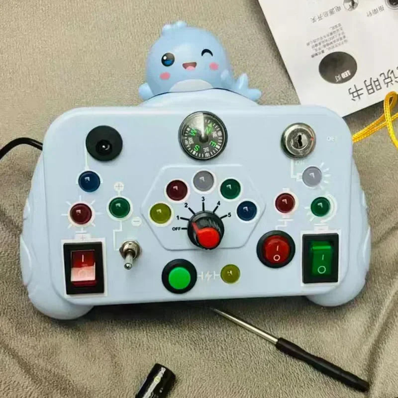Light blue activity board with a character topper, colorful buttons, switches, a key, and a central dial