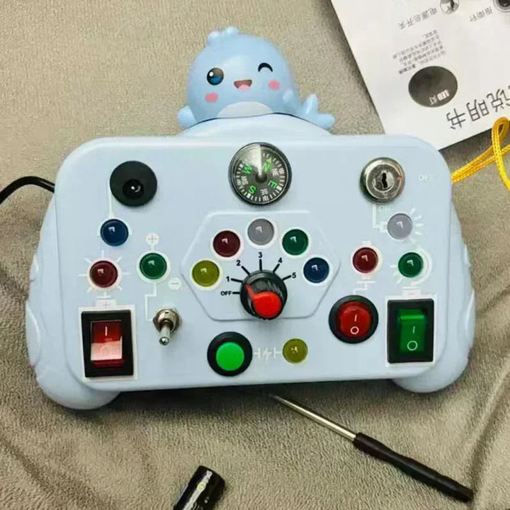 Light blue activity board with a character topper, colorful buttons, switches, a key, and a central dial