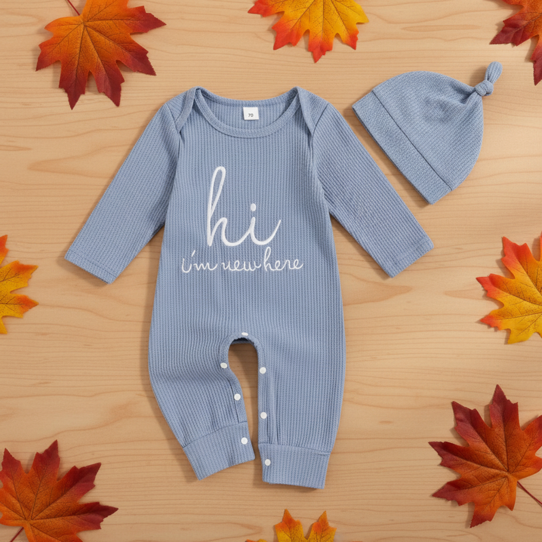 Light blue baby jumpsuit and knotted beanie arranged on wood with autumn leaves