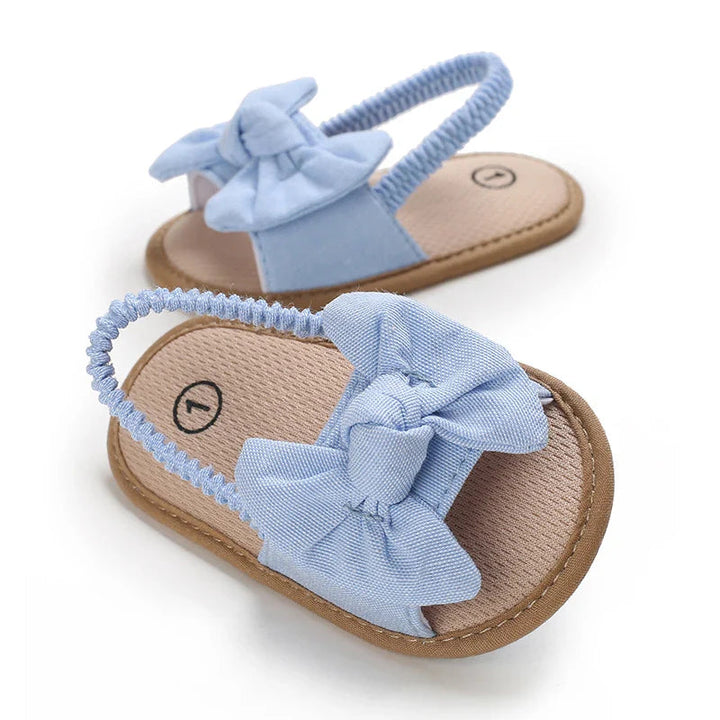 Light blue bow baby sandals with tan footbeds shown at an angle