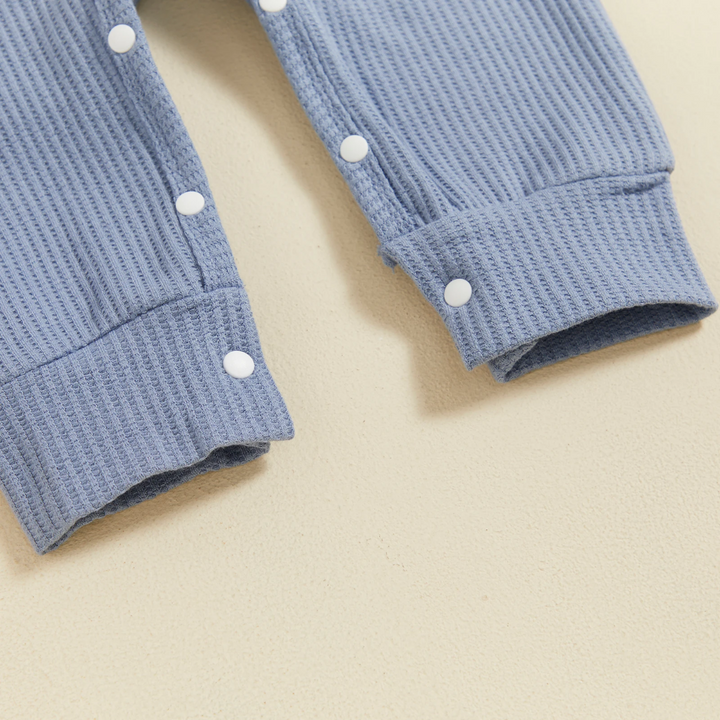 Close-up of white leg snaps, ribbed fabric and ankle cuffs on the light blue baby jumpsuit