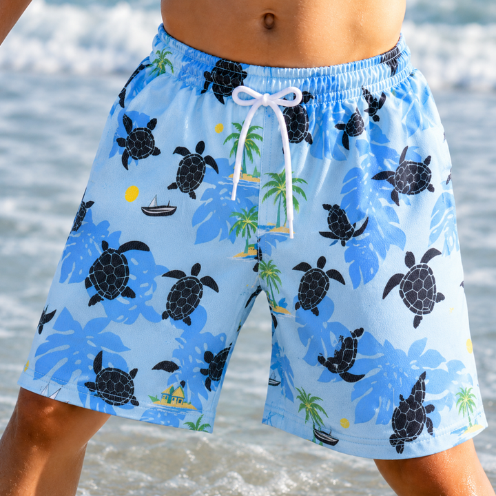 Front view of light blue swim trunks with black turtles, green palms, and a white drawstring