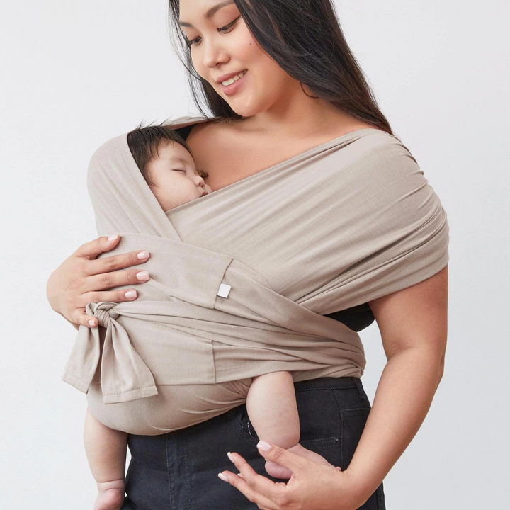 Parent carrying a baby against the chest in a light gray wrap-style carrier