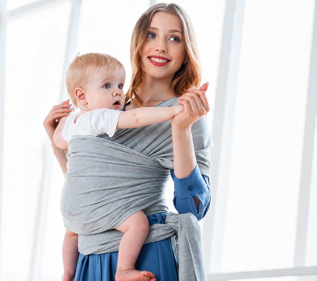 Light gray baby wrap carrier worn by a parent indoors with a baby facing inward.