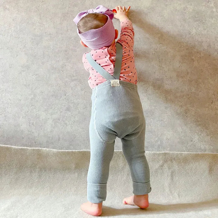 Baby wearing light gray ribbed leggings with crossed suspenders