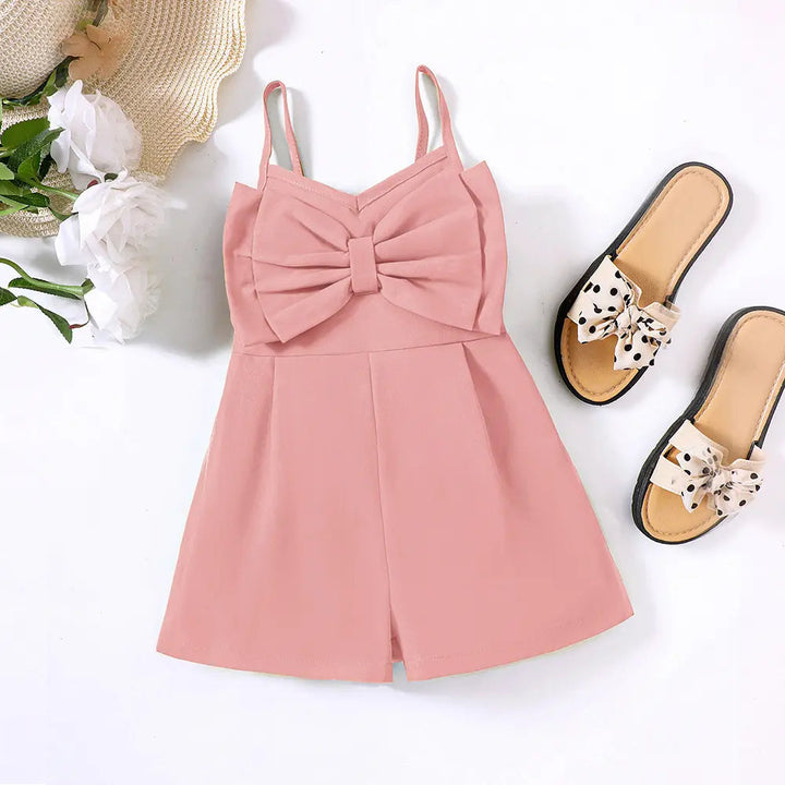 Light pink bow-front romper styled beside sandals, white flowers and a straw hat