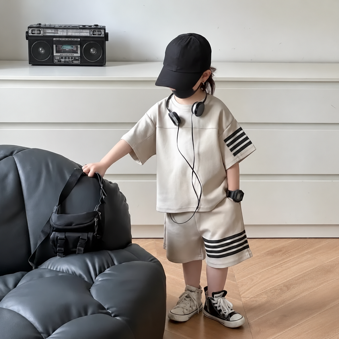 Child standing beside a sofa in a light-colored T-shirt and shorts set with dark stripes.