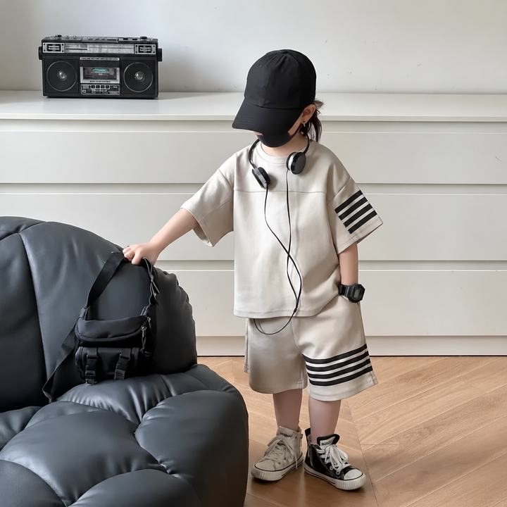 Child standing beside a sofa in a light-colored T-shirt and shorts set with dark stripes.