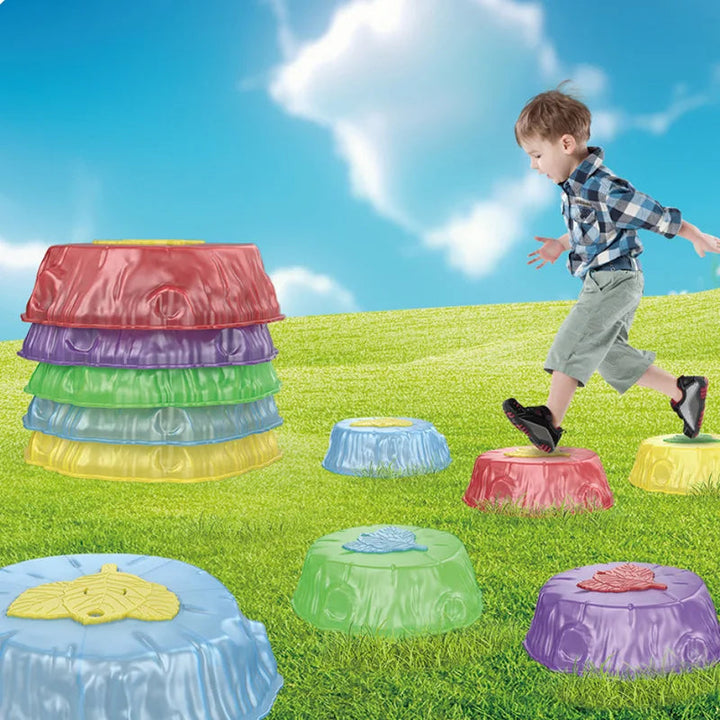 Child stepping across colorful balance stones on grass beside a stack of stones