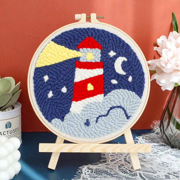 Lighthouse punch needle hoop with waves, a crescent moon, and a yellow beam of light