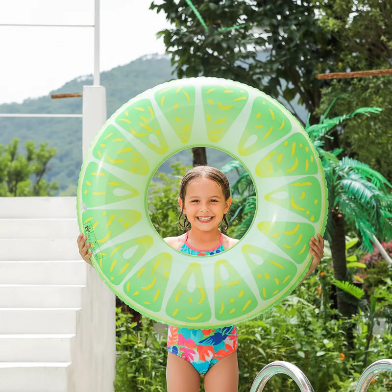 Child holding a lime-slice swim ring beside an outdoor pool.