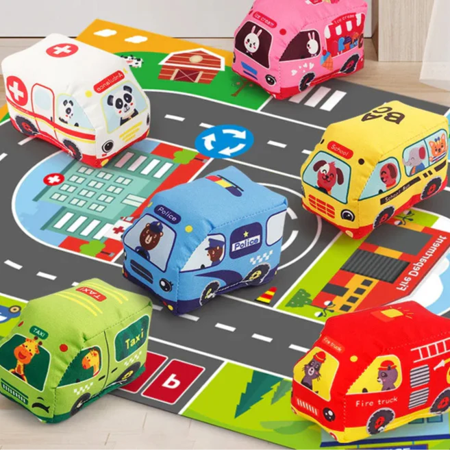 Six colorful soft vehicles arranged on a city road play mat with crossings and a roundabout