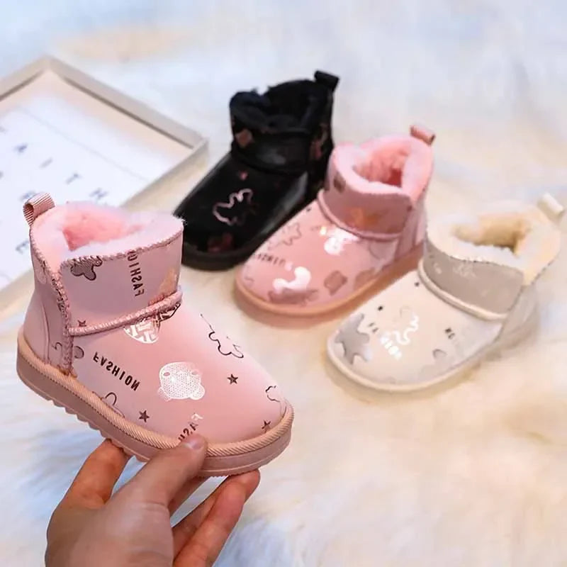 Pink printed kids' snow boot held in front of black, pink, and beige boots