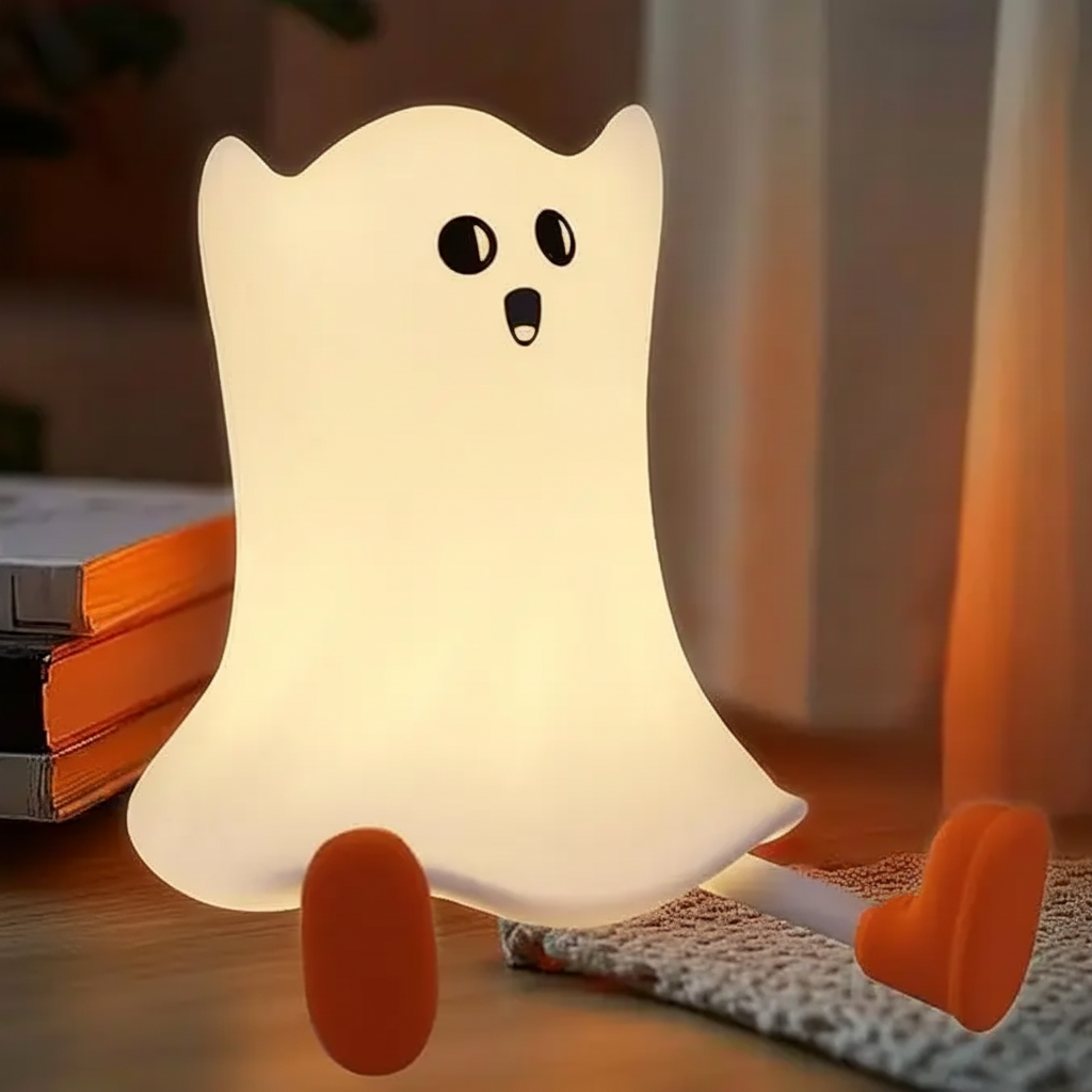 Little ghost night light glowing beside books with its orange feet outstretched