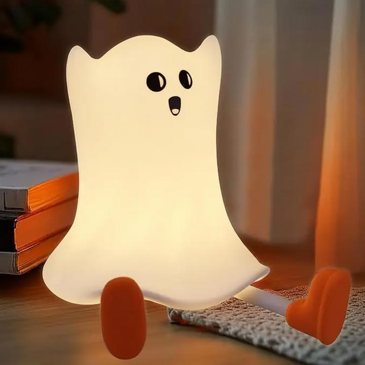 Little ghost night light glowing beside books with its orange feet outstretched