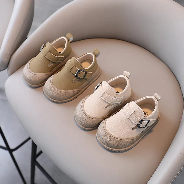 Khaki and beige baby shoes with buckle details arranged in pairs on a chair