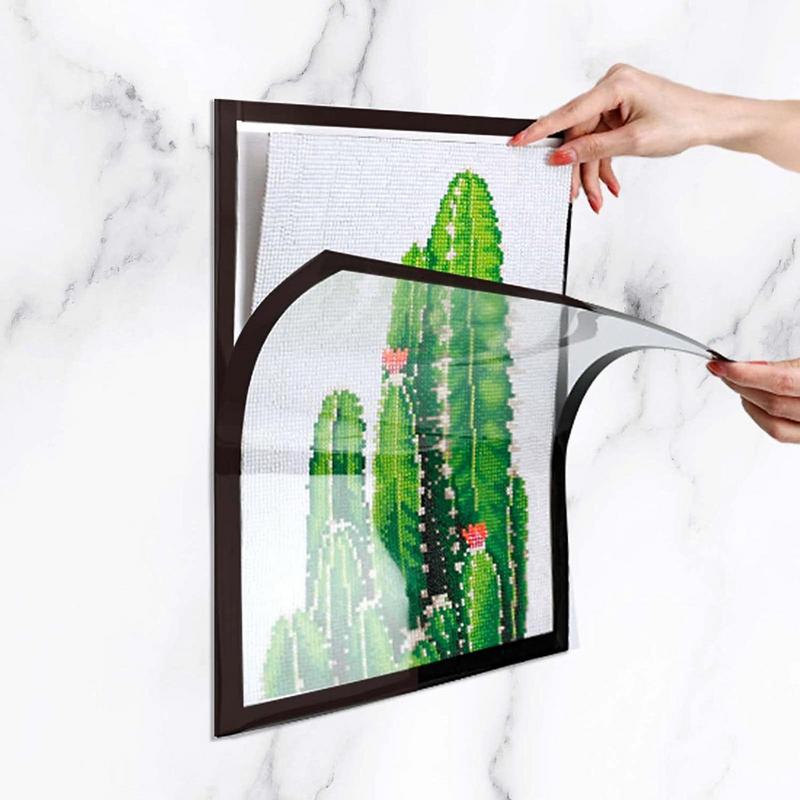 Hands lift the flexible magnetic front of a black frame holding cactus artwork on a wall
