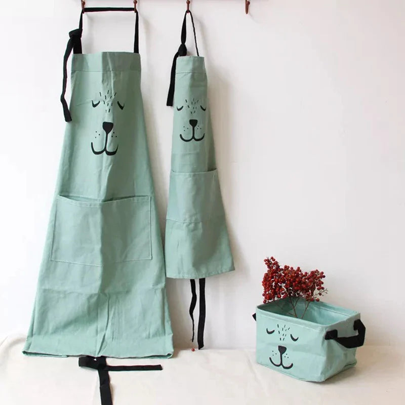 Matching green bear aprons in adult and child sizes displayed on wall hooks