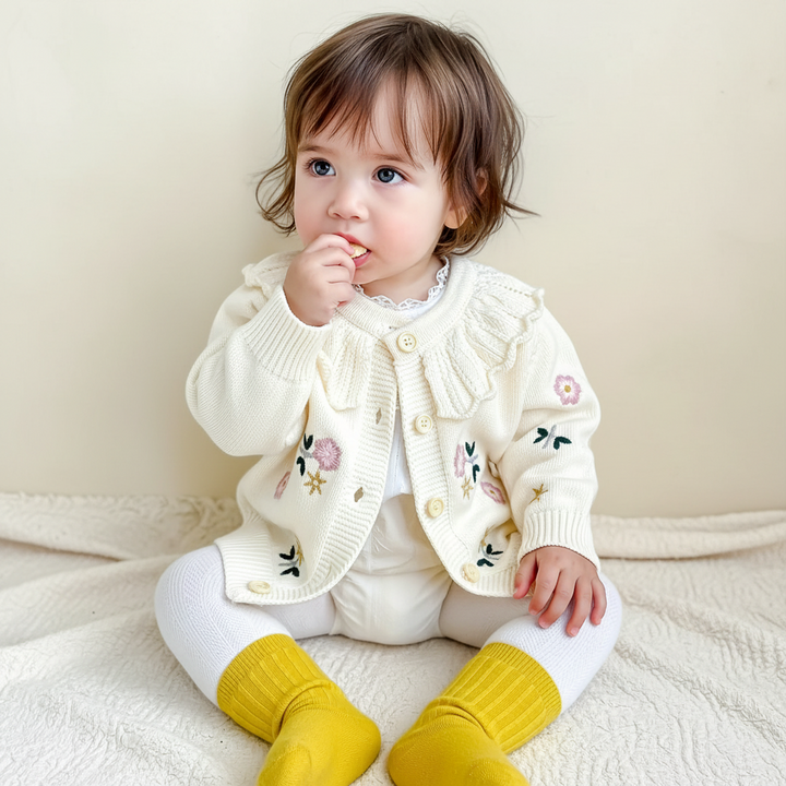 Seated child wearing the cream floral cardigan with yellow socks