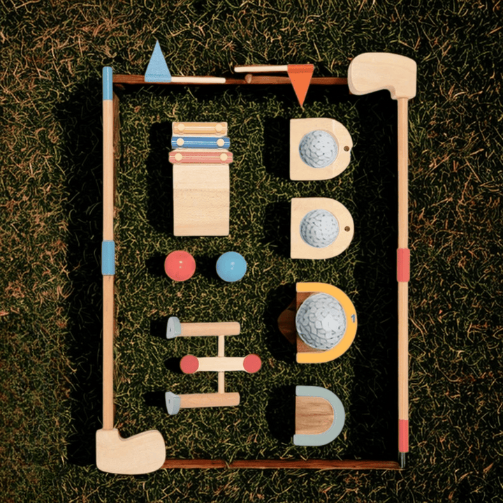Wooden golf set arranged on grass with two clubs, two balls, flags, targets and obstacles