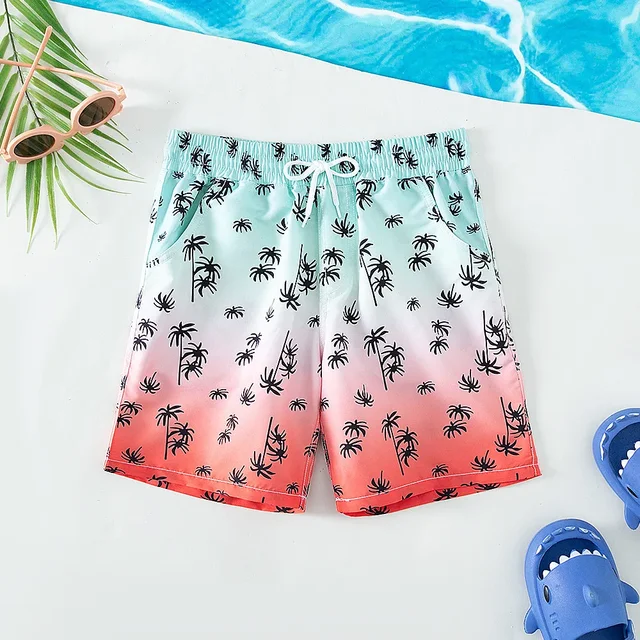Mint-to-coral palm-print swim trunks with an elastic waist and white drawstring beside a pool.