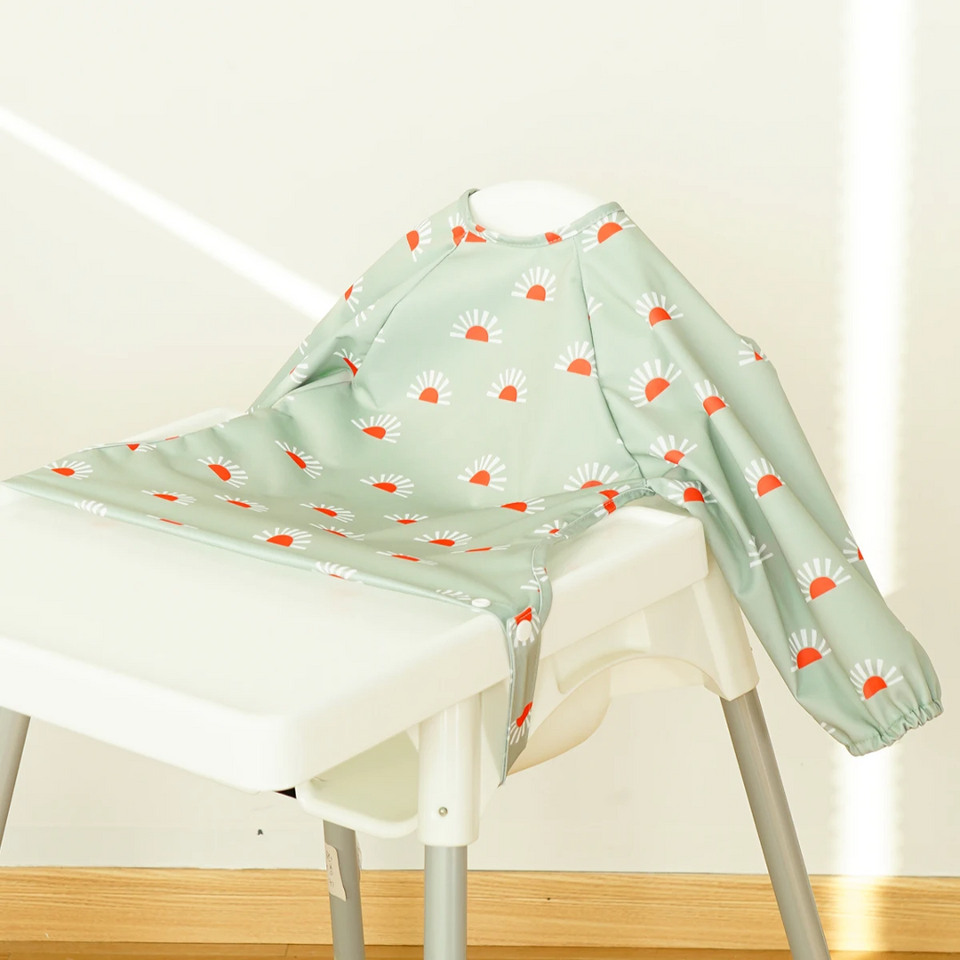 Mint green long-sleeve baby bib with orange-and-white flower motifs on a high chair