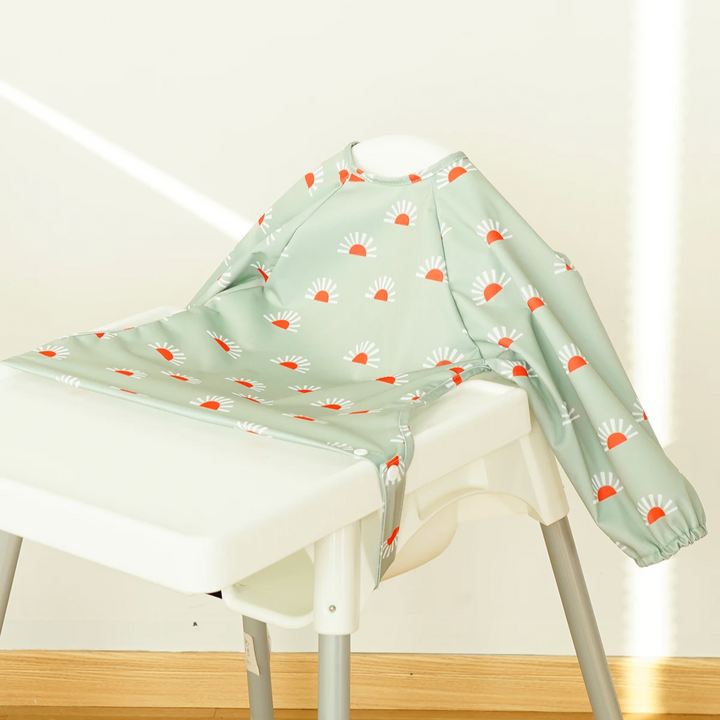Mint green long-sleeve baby bib with orange-and-white flower motifs on a high chair