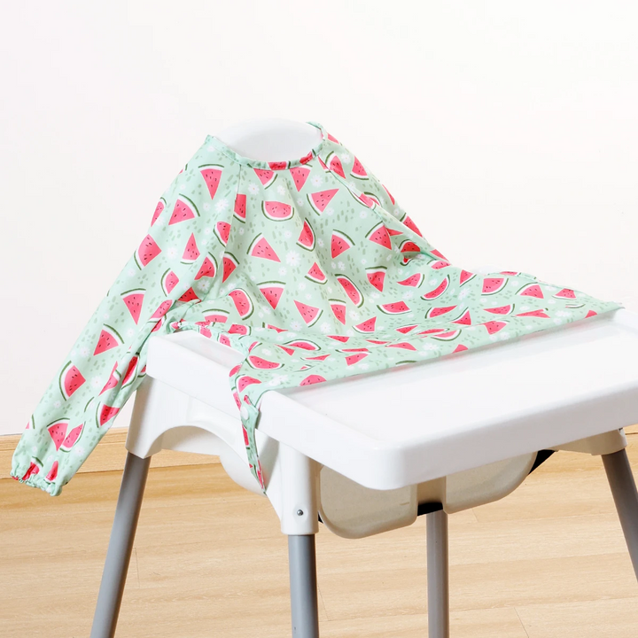 Mint green long-sleeve baby bib with watermelon slices displayed on a high chair
