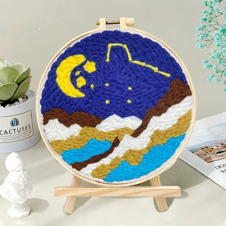 Moon and stars punch needle hoop above a layered mountain-and-water landscape