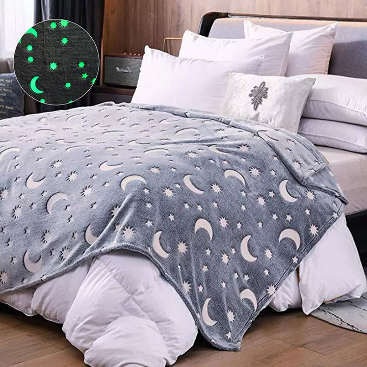 Gray sun, moon, and star blanket on a bed with an inset showing the glowing pattern