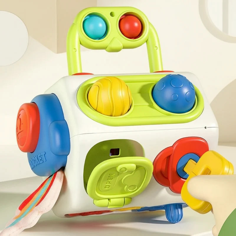Colorful activity cube with a raised green handle, turning controls, a hinged door, and a yellow play key