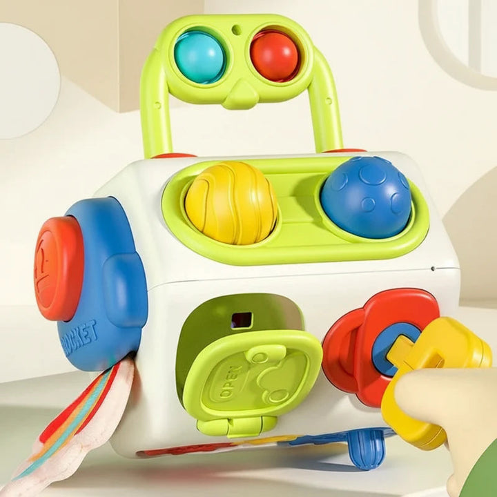Colorful activity cube with a raised green handle, turning controls, a hinged door, and a yellow play key
