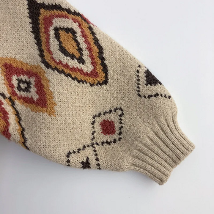 Red, yellow, and brown diamond details along a beige sweater sleeve with a ribbed cuff