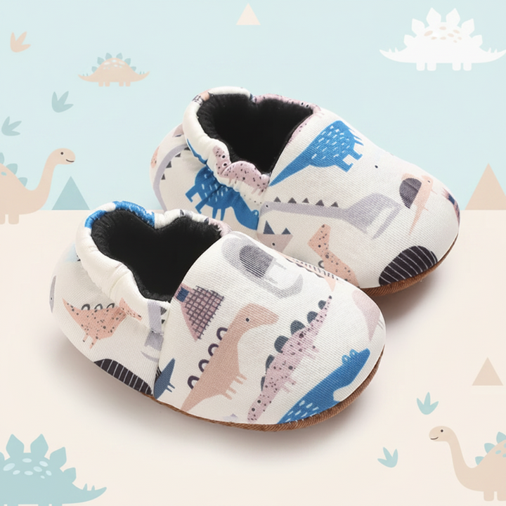 White baby shoes covered in blue, pink and gray dinosaur prints.