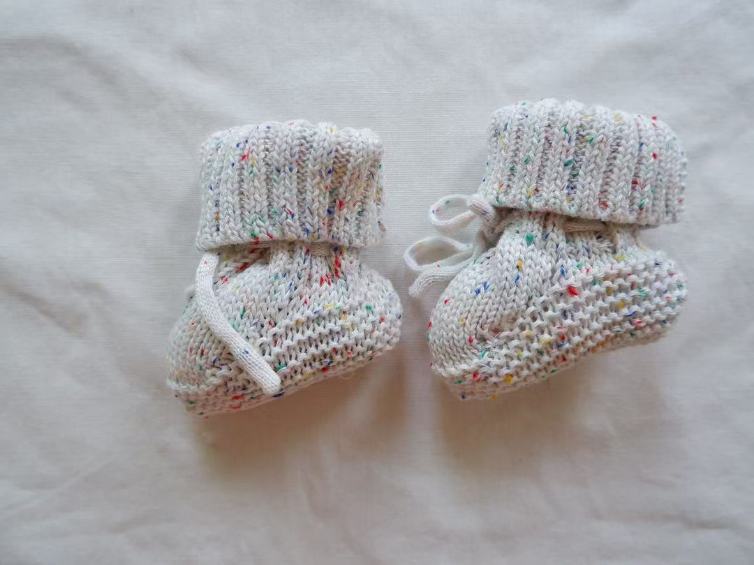 Multicolor-flecked baby booties with folded ribbed cuffs and white ankle ties.