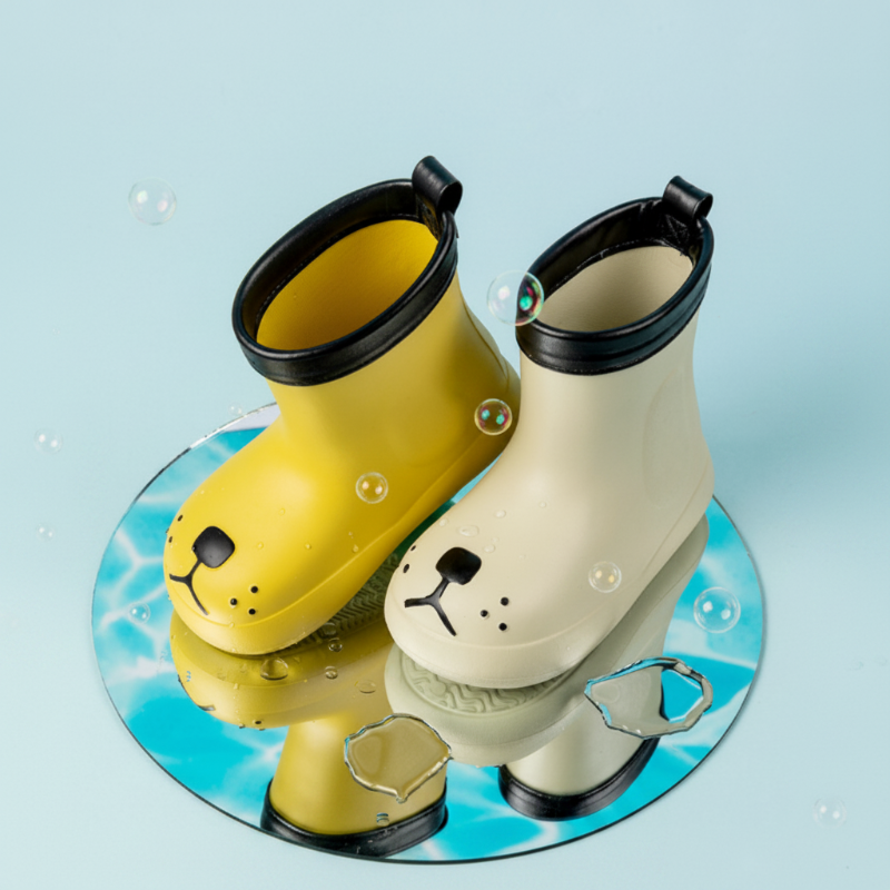Mustard and cream dog-face rain boots with black top rims on a reflective blue display