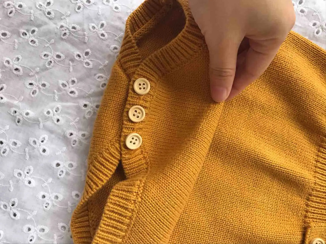 Close-up of mustard yellow knit fabric, ribbed edging, and three small buttons