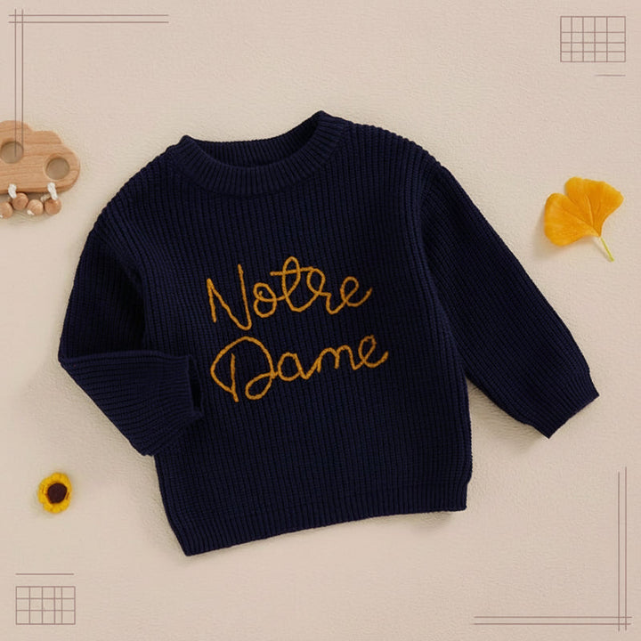 Navy blue script-embroidered sweater laid flat with one sleeve folded.