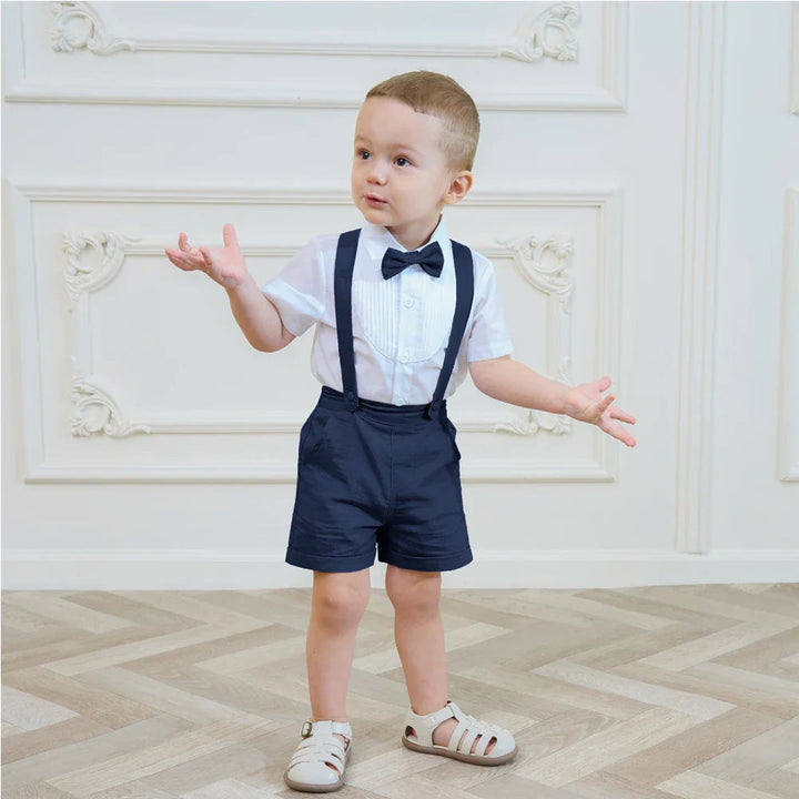 Boy wearing a navy suspender shorts set and white short-sleeve shirt with his arms out