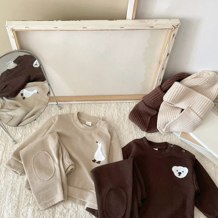 Beige goose and brown bear outfits arranged with matching pants and neutral accessories