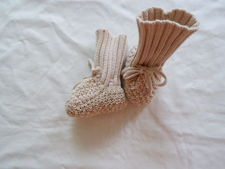 Light neutral baby booties with ankle ties, showing one tall cuff and one folded cuff.