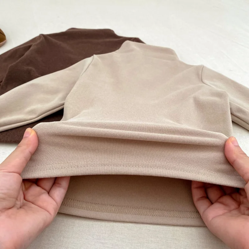Close-up of the fabric and inside hem of a neutral long-sleeve baby sweater.
