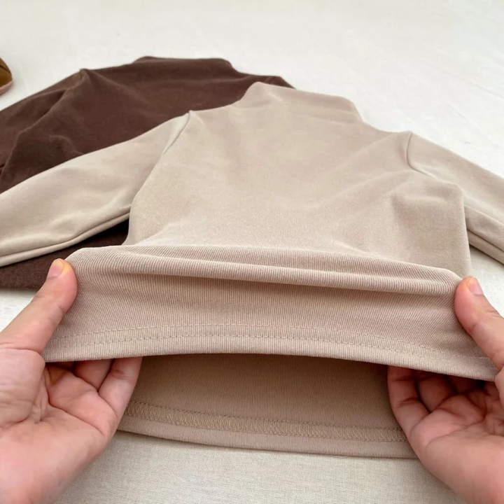 Close-up of the fabric and inside hem of a neutral long-sleeve baby sweater.
