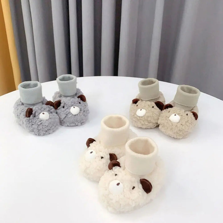 Gray, cream, and khaki bear baby slippers arranged on a round white table