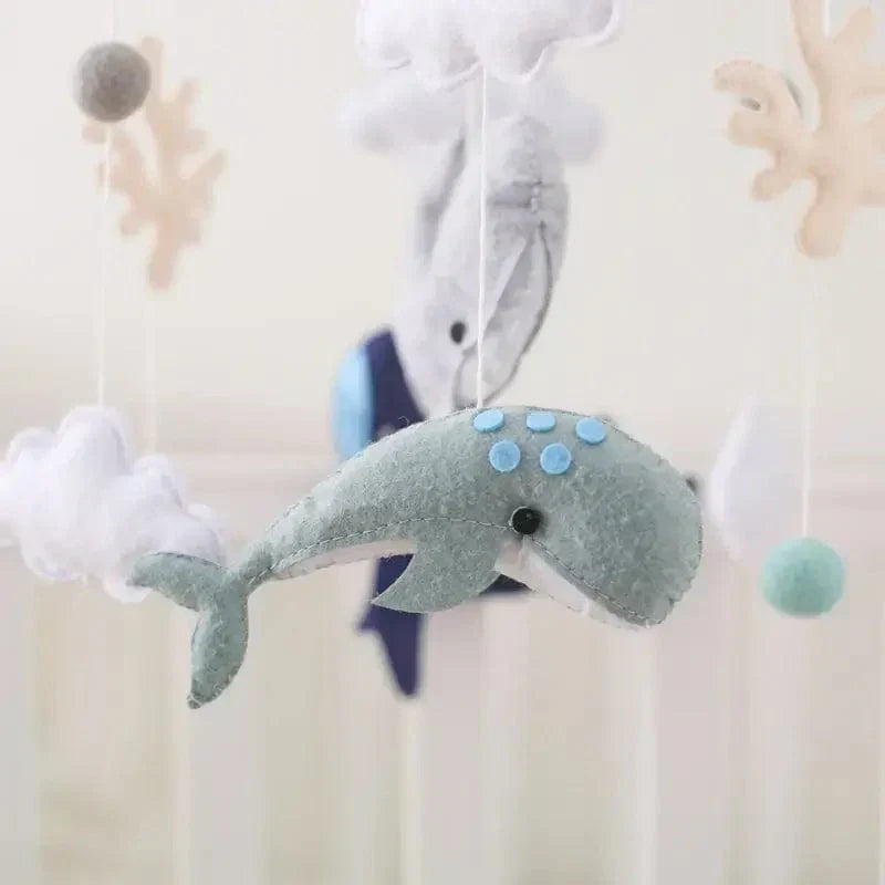 Close-up of a teal felt whale with blue spots, surrounded by clouds and other hanging figures