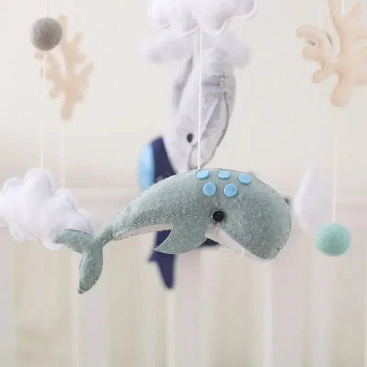 Close-up of a teal felt whale with blue spots, surrounded by clouds and other hanging figures